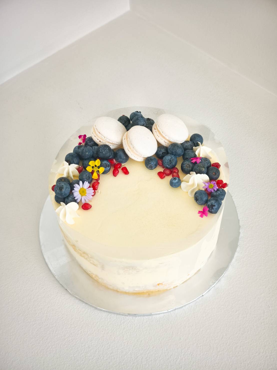 Vanilla cream cake decorated with fresh blueberries, white macarons, edible flowers, and red berries.