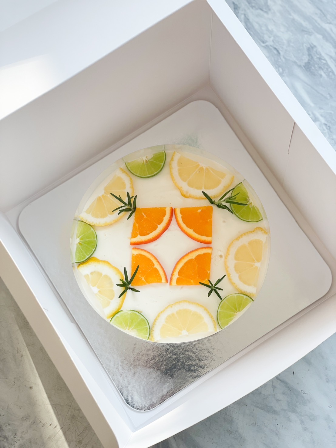 A light and refreshing citrus jelly cake, beautifully decorated with lemon, lime, and orange slices, topped with rosemary sprigs for a fresh and elegant look.