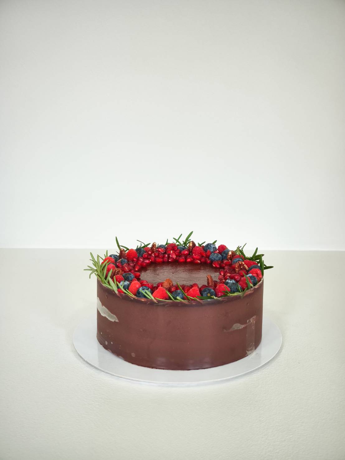 Elegant dark chocolate cake topped with fresh strawberries, blueberries, raspberries, red currants, and rosemary