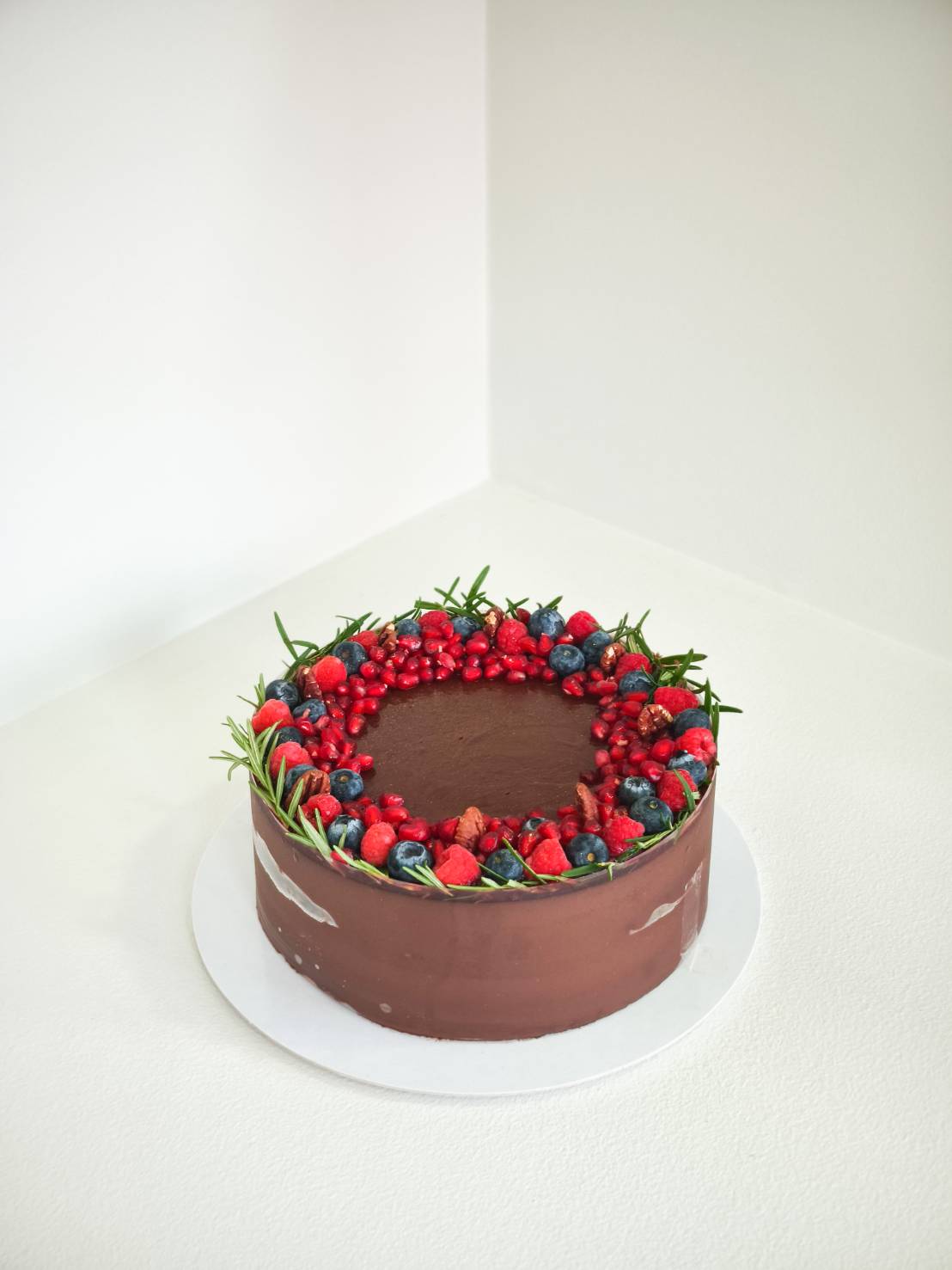 Dark chocolate cake with wreath-style topping of strawberries, blueberries, raspberries, red currants, pomegranate seeds, and rosemary