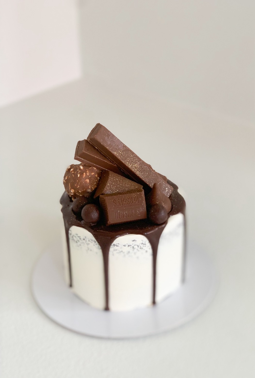Mini chocolate drip cake topped with assorted chocolates including KitKat, Ferrero Rocher, Hershey’s, and chocolate balls.