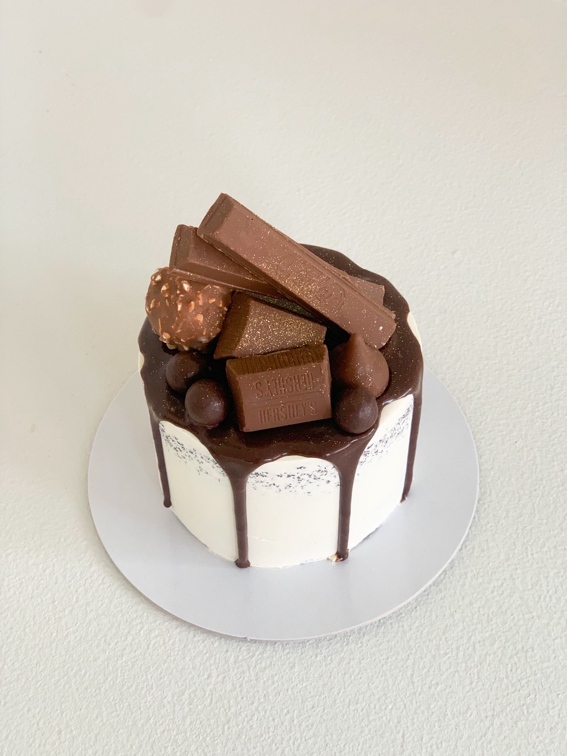 Mini chocolate drip cake topped with assorted chocolates including KitKat, Ferrero Rocher, Hershey’s, and chocolate balls.