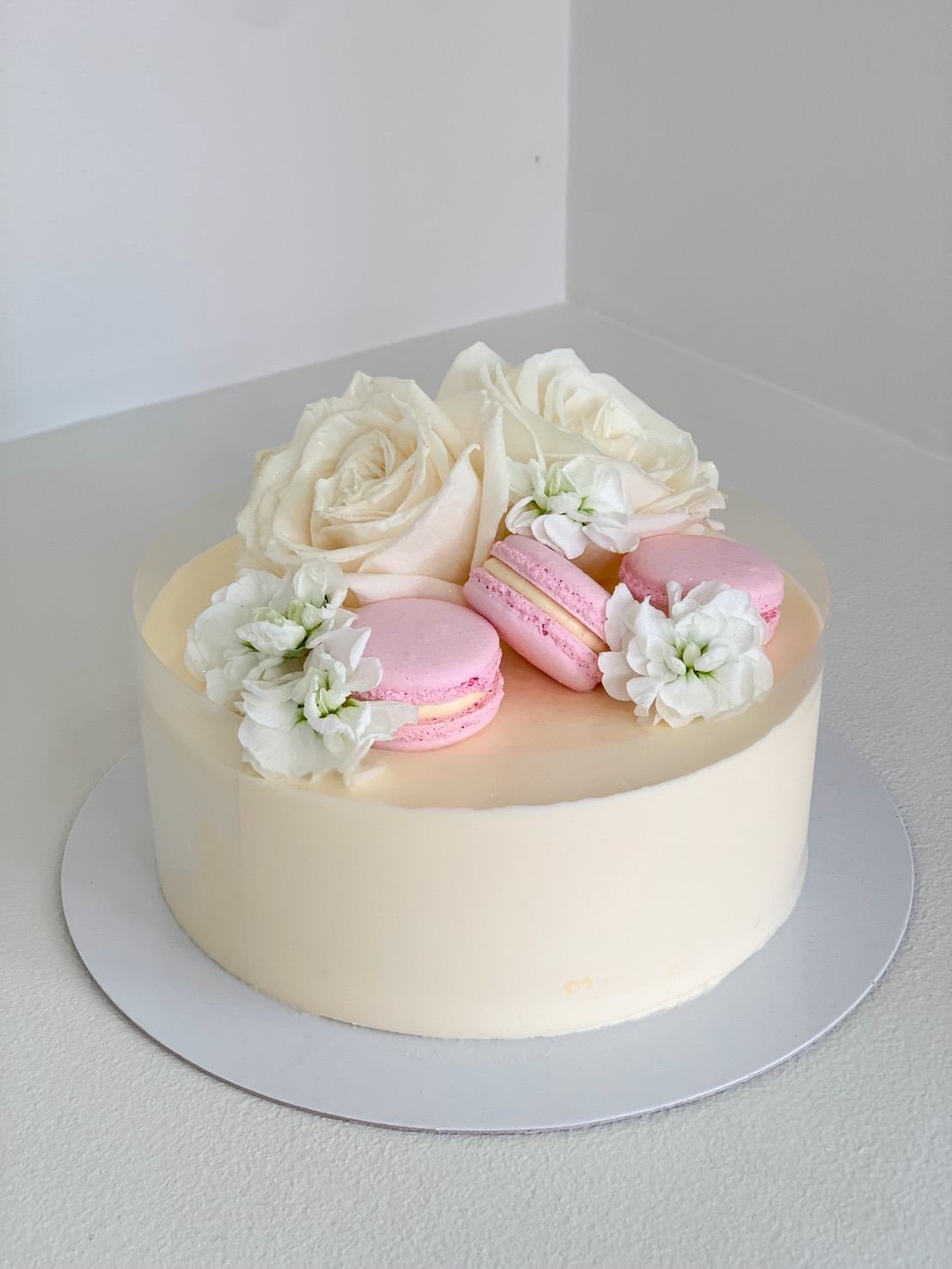 Elegant round vanilla cake topped with white roses, pink macarons, and delicate white flowers.