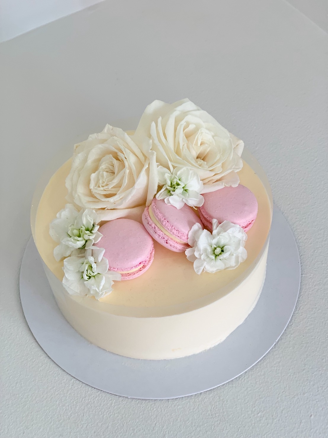 Top view of a white vanilla cake with pink macarons, white roses, and fresh white flowers arranged elegantly.