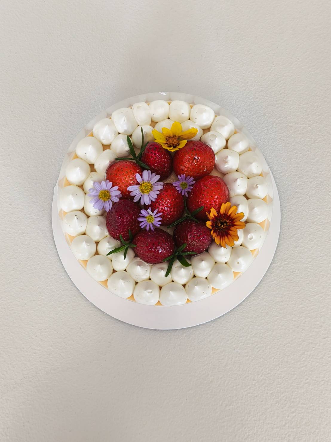 Fresh strawberry cake topped with whole strawberries, edible flowers, and piped cream swirls, arranged beautifully on a round cake base.