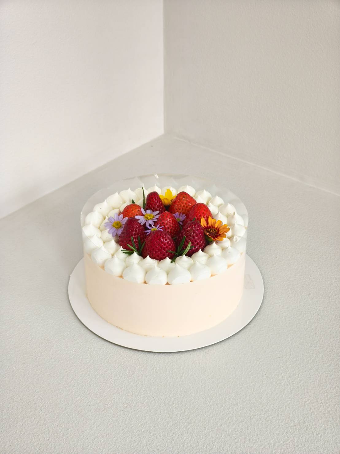 resh strawberry cake topped with whole strawberries, edible flowers, and piped cream swirls, arranged beautifully on a round cake base.