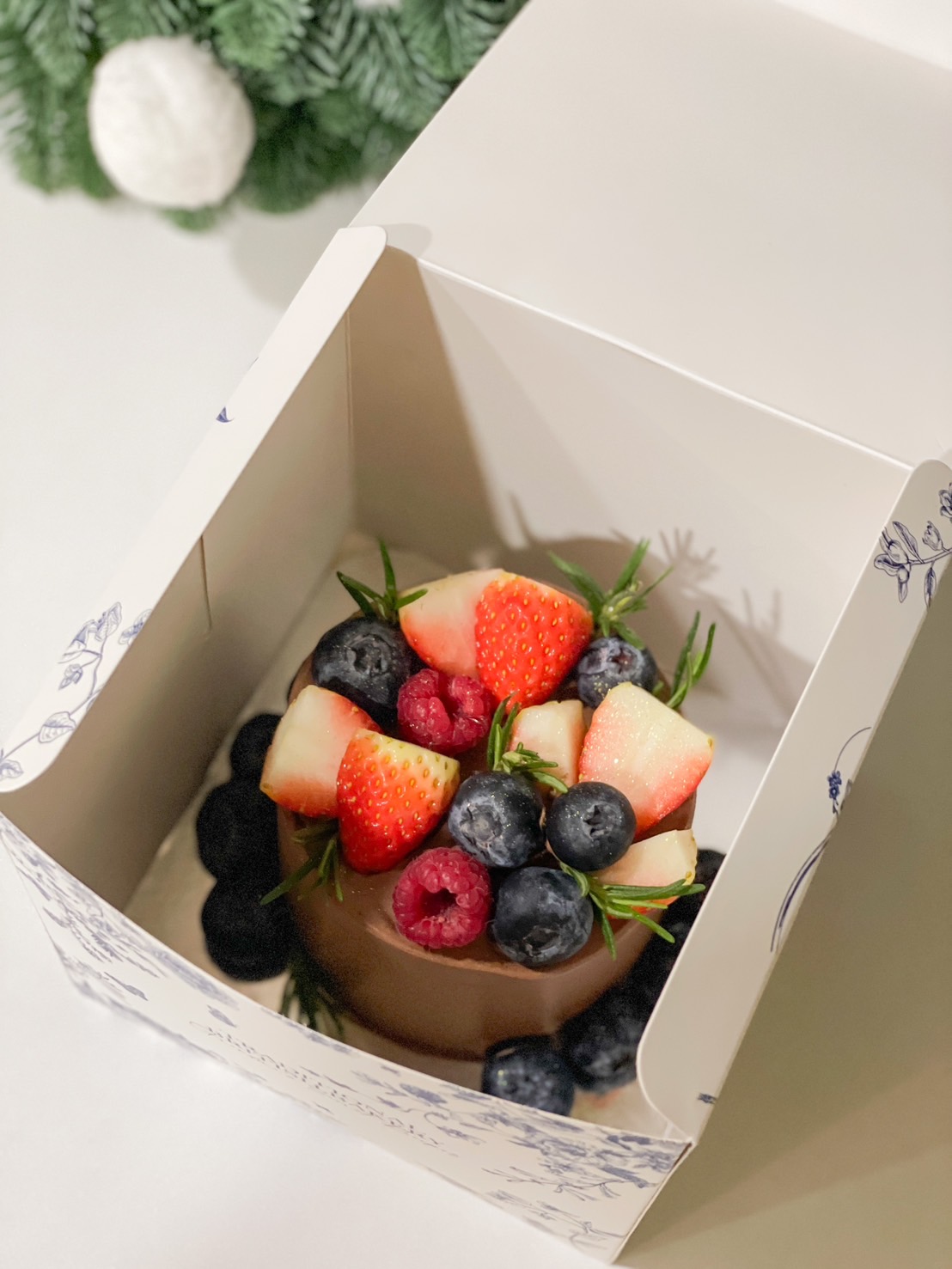 Mini cake decorated with fresh strawberries, blueberries, and raspberries in a gift box by Basketeer.