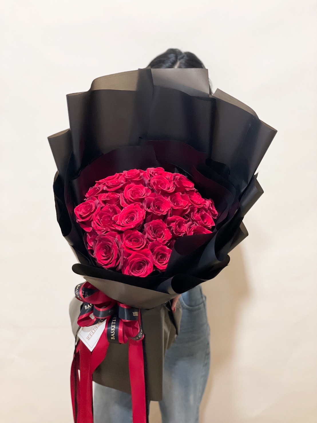 A luxurious bouquet of 50 red roses, wrapped in sleek black paper with a deep red ribbon for an elegant and passionate floral arrangement.