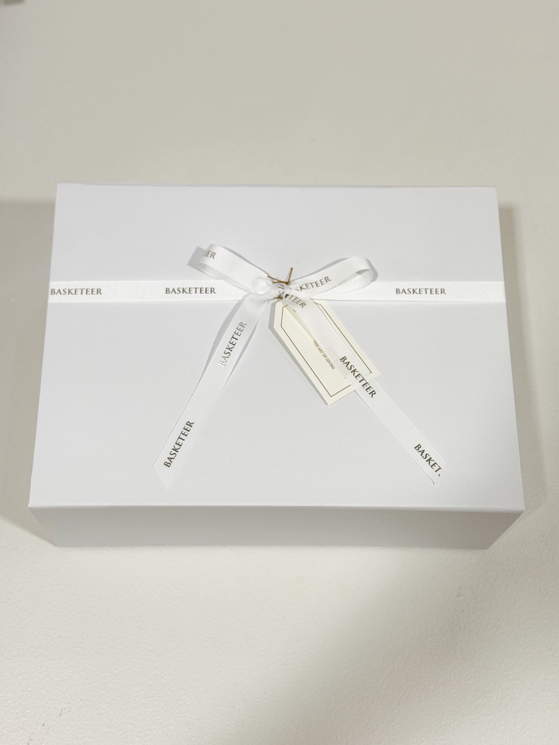 Elegant white gift box tied with white “Basketeer” ribbon and gift tag, luxury packaging for premium presents.