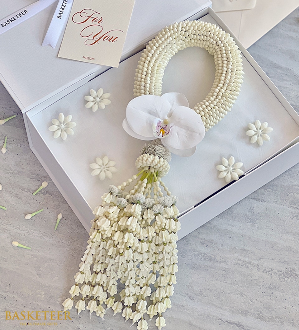 A white jasmine garland with a white orchid in the center, presented in a white box with the word 