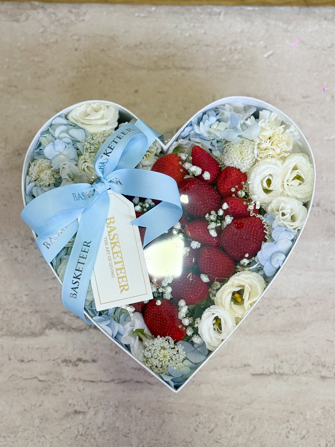 A luxurious heart-shaped box brimming with vibrant strawberries and elegant white roses, finished with a signature Basketeer ribbon.