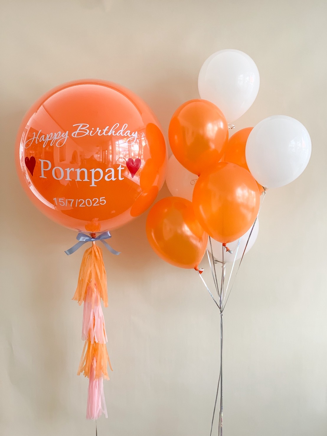 Personalised orange birthday balloon with name “Pornpat” and date, paired with matching orange and white helium balloons.