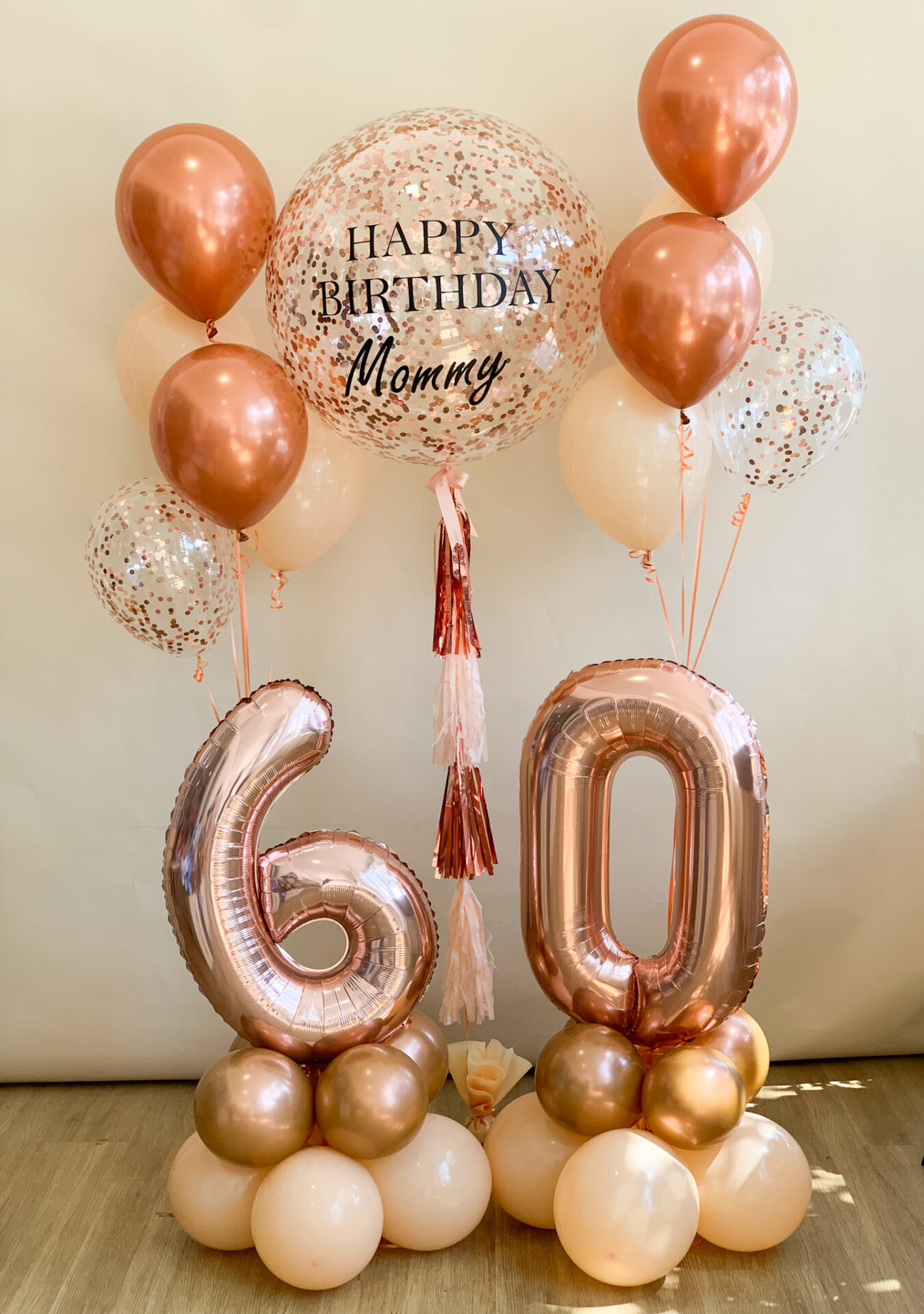 A stunning rose gold birthday balloon arrangement with a personalized confetti balloon, number balloons for age 60, and matching helium balloons, perfect for milestone celebrations.