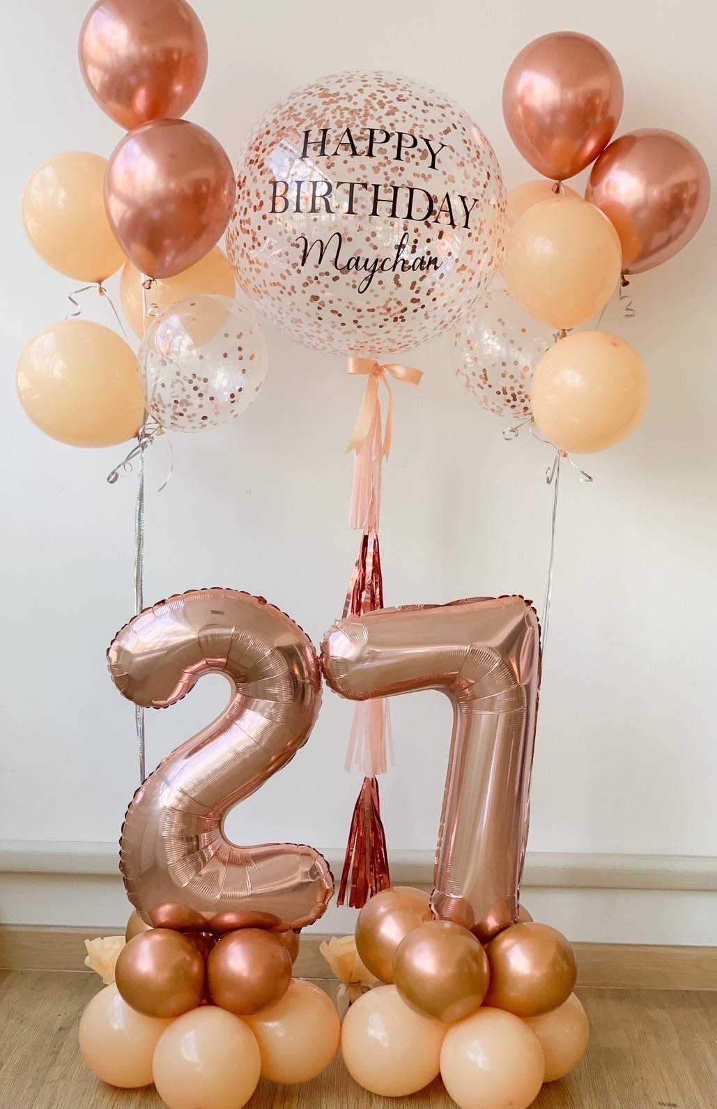 A balloon display for a 27th birthday celebration featuring a large, confetti-filled balloon with 