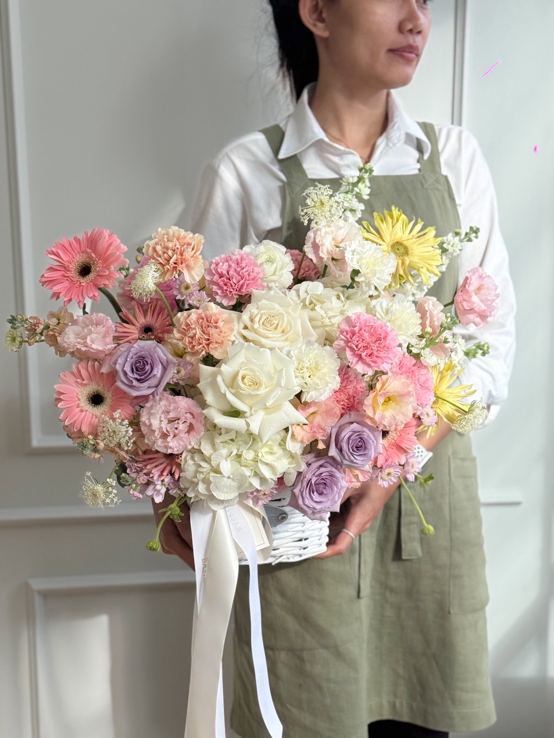 Pastel flower basket with white roses, hydrangeas, carnations, gerberas, and soft pink and lavender blooms, tied with ribbon