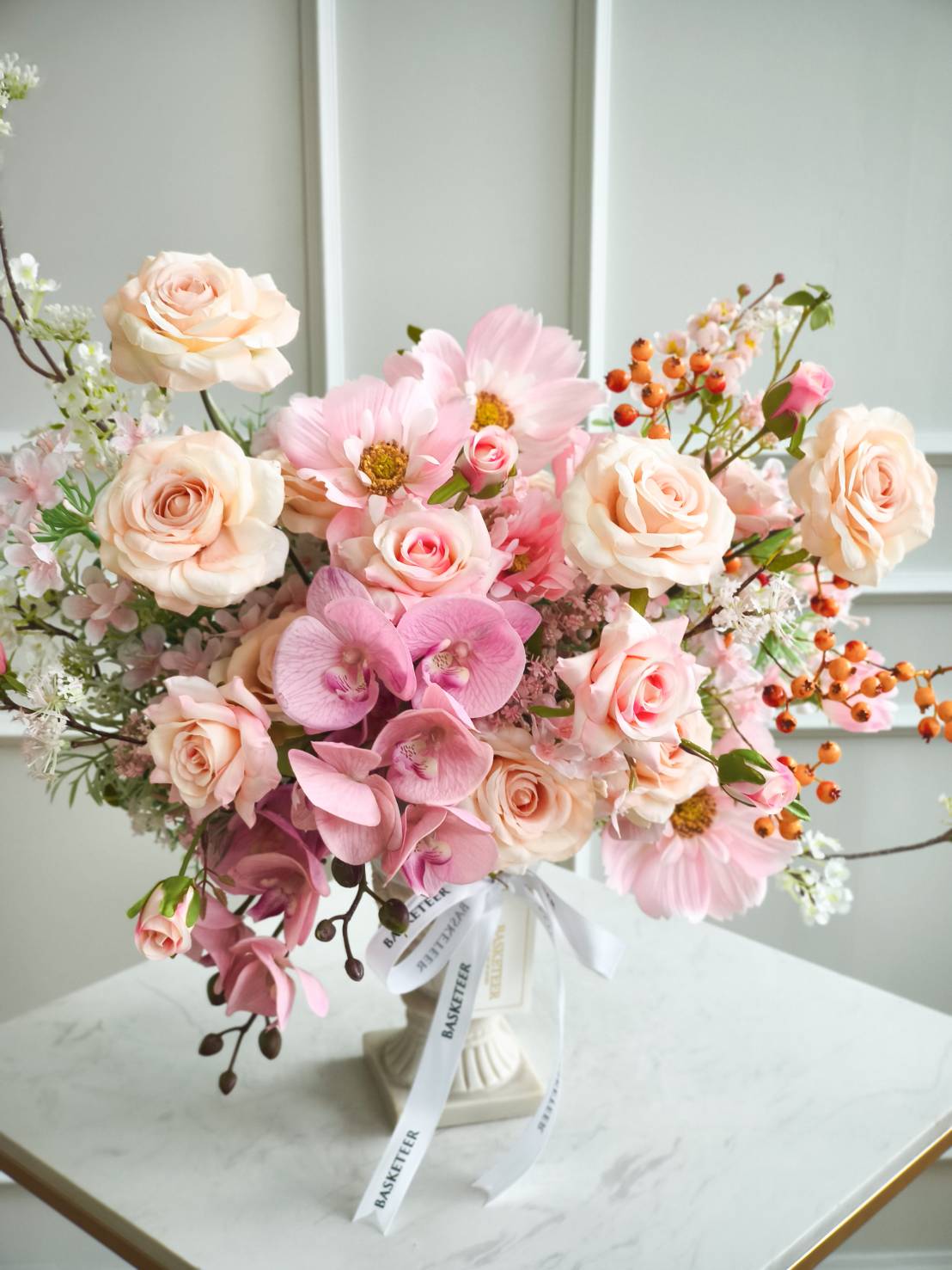 Luxury vase with peach roses, pink orchids, cosmos flowers, and pastel blooms, decorated with white satin ribbon