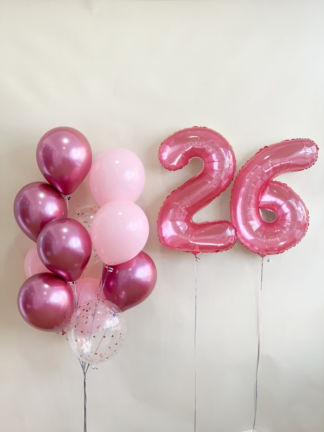 A pink birthday balloon bouquet featuring metallic pink, pastel pink, and rose gold balloons with large foil number 26.