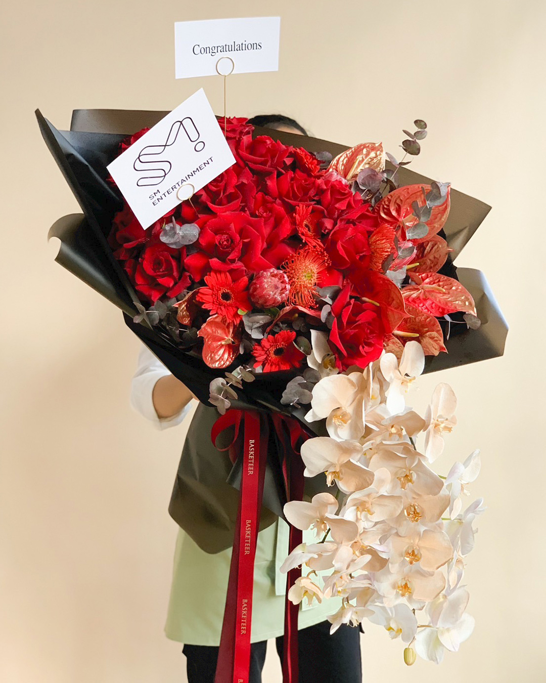 Luxury red and white congratulatory flower bouquet from BASKETTER with red roses, white orchids, red gerberas, and a “Congratulations” card tied with a red ribbon.
