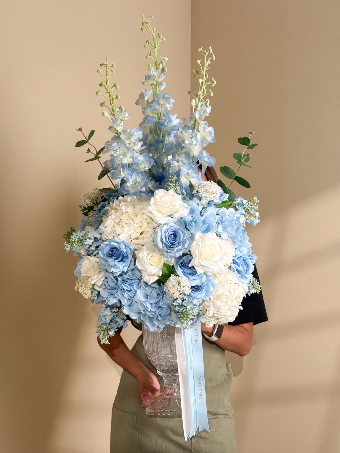 Elegant blue and white flower arrangement in a tall clear glass vase with roses, hydrangeas, and delphiniums – luxury floral decor.
