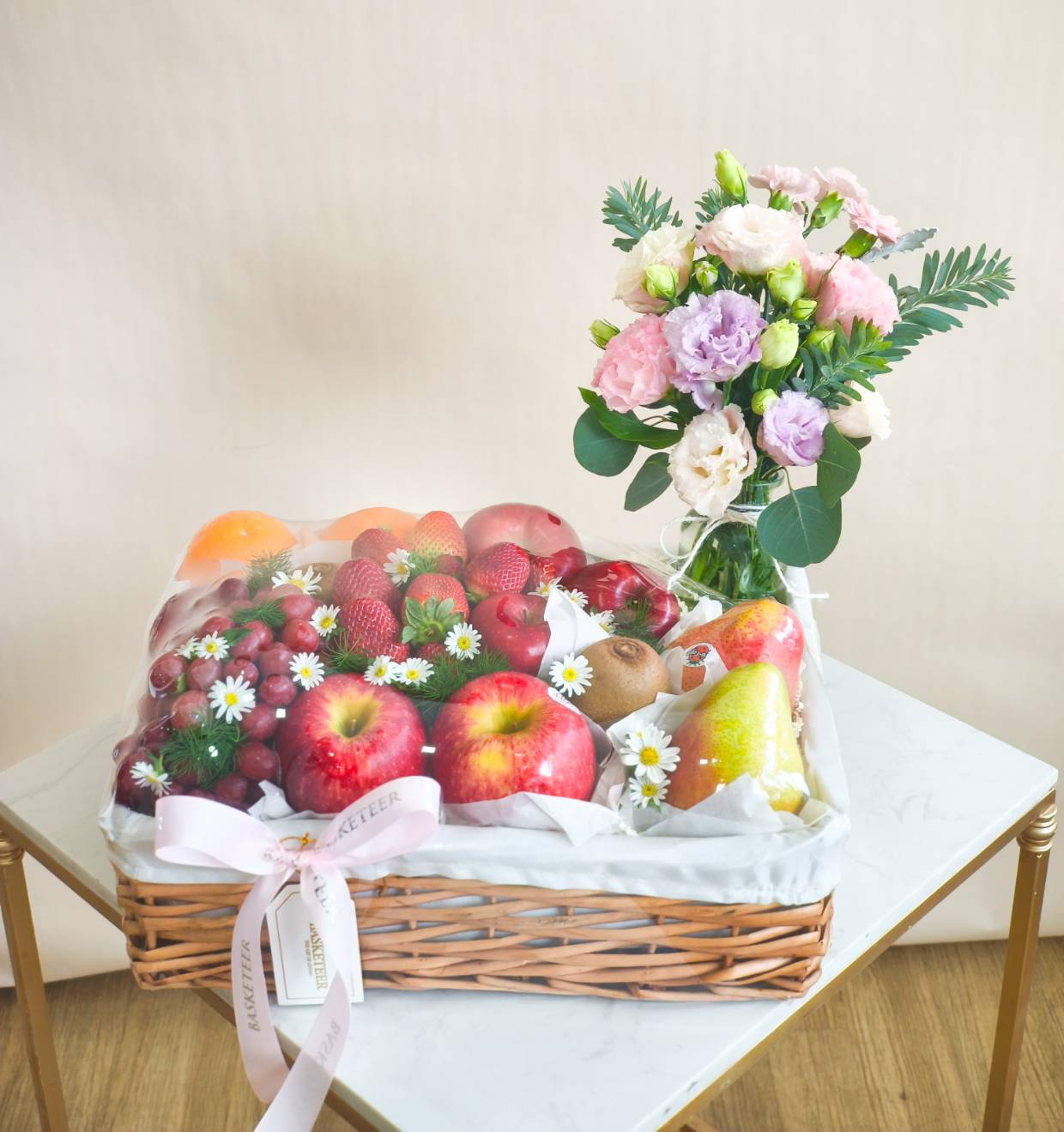Luxury fruit basket with apples, pears, strawberries, grapes, oranges, kiwi, decorated with daisies, paired with pastel flower vase.