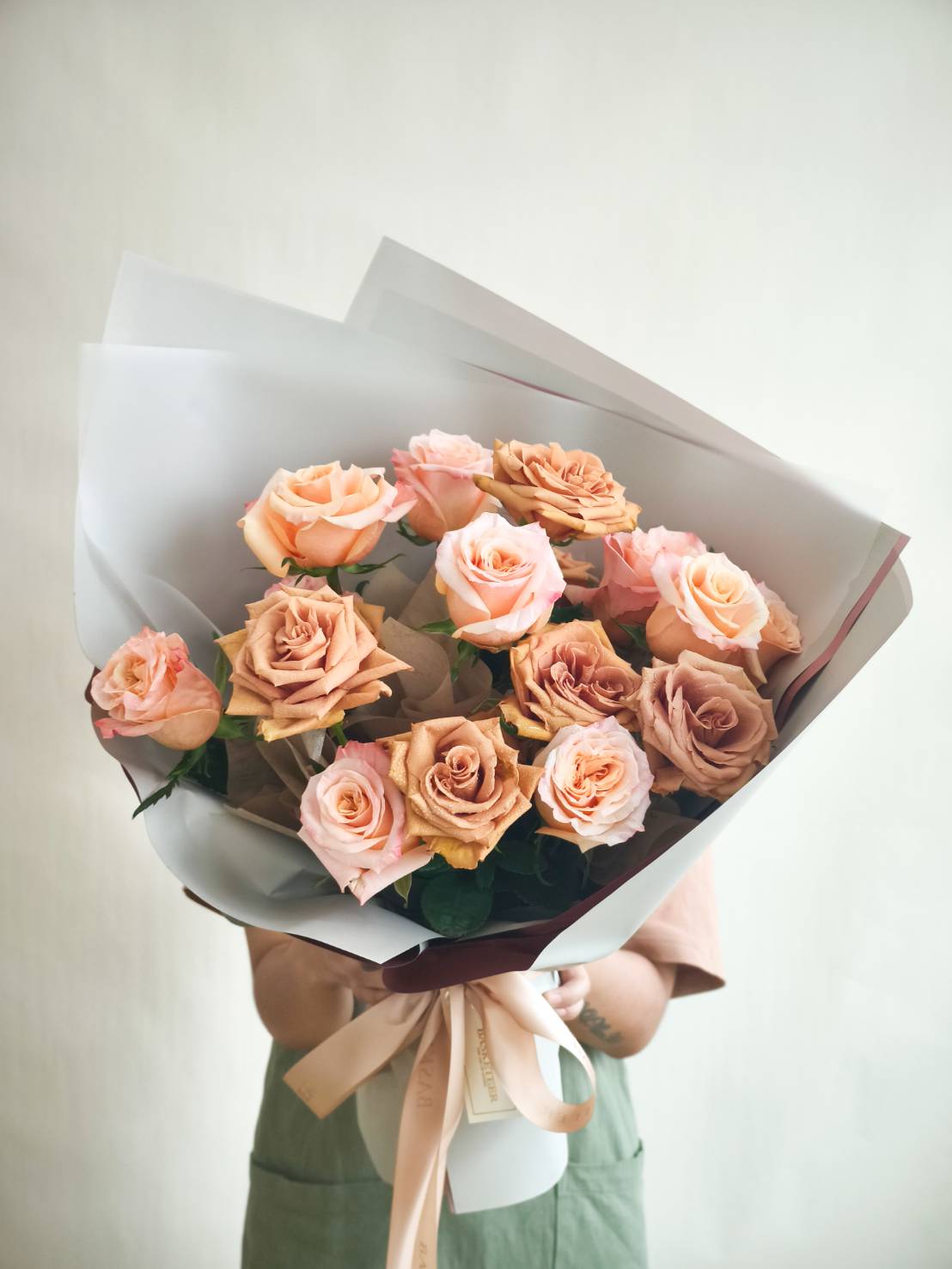 Luxury bouquet of peach and toffee roses wrapped in elegant white paper with satin ribbon.