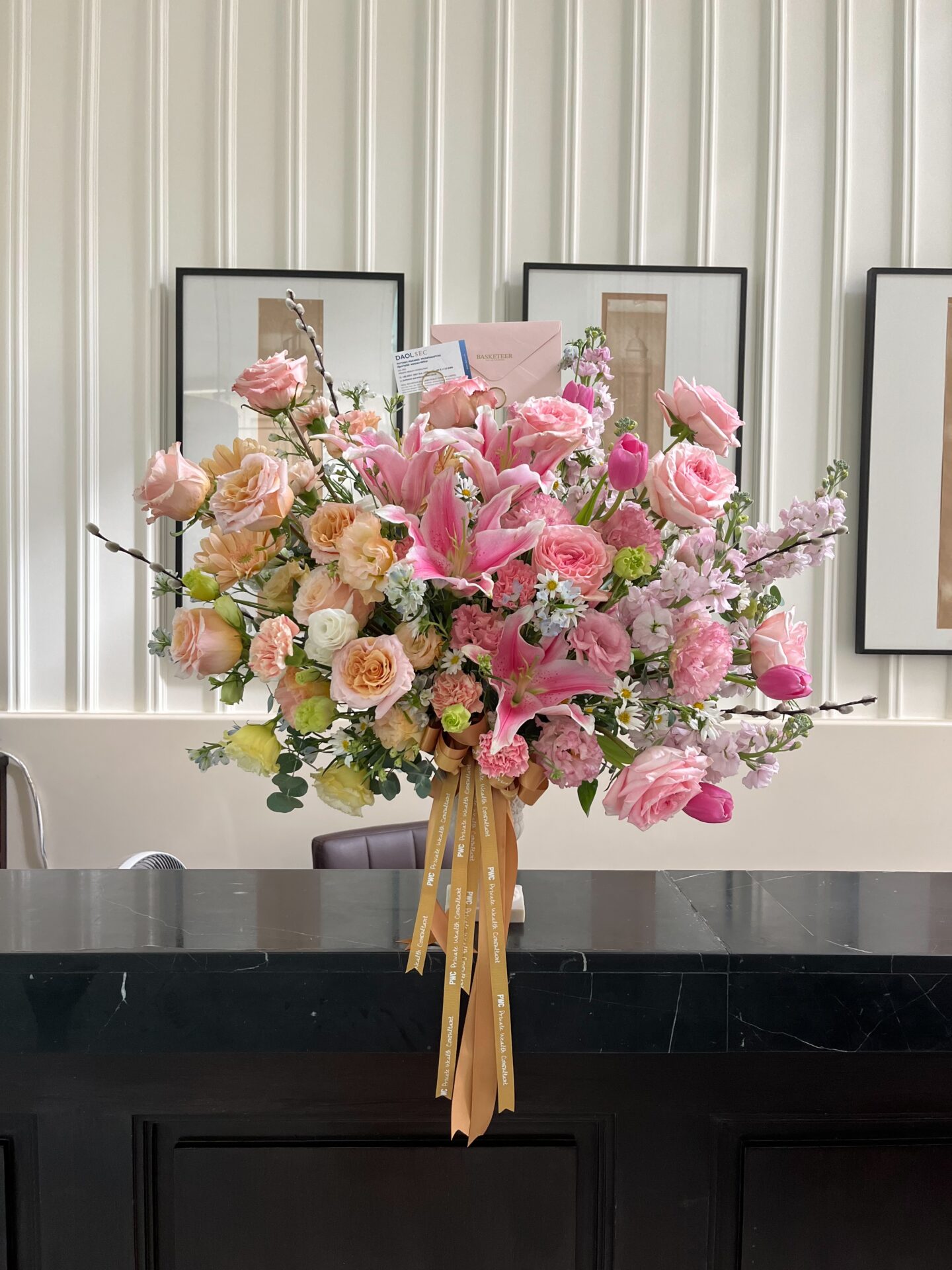 Elegant pink and peach flower arrangement in a vase placed on a black marble reception counter, featuring lilies, roses, and carnations.