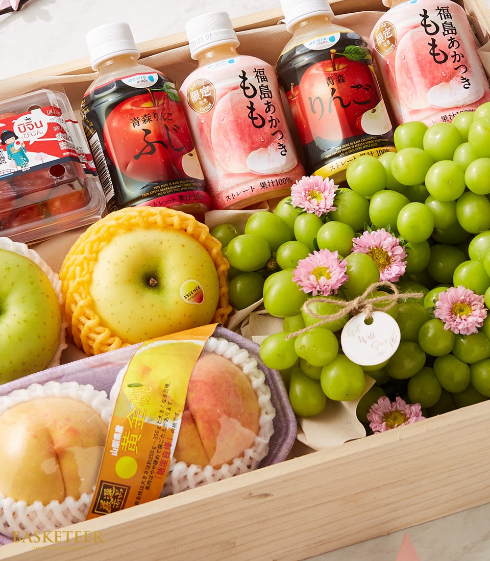 The Basketeer Premium Fruit Box Elysium exudes luxury and sophistication within a beautifully crafted wooden gift box. This exquisite selection features two golden-yellow apples, a lush cluster of emerald green grapes, and two impeccably boxed juicy peaches. Adding an element of sweetness are vibrant red jelly cups, alongside three elegant bottles of peach and grape beverages. Adorned with delicate pink flowers for an enchanting touch, the box showcases the brand's logo on both its ribbon and packaging, inviting you to indulge in this extraordinary gourmet experience.