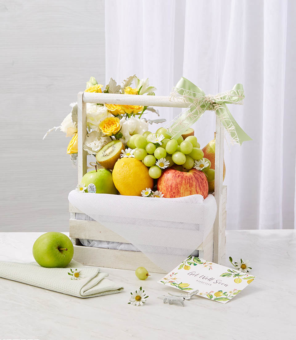 Fresh Fruits In The White Wooden Basket With A Small Yellow And White Flowers Vase