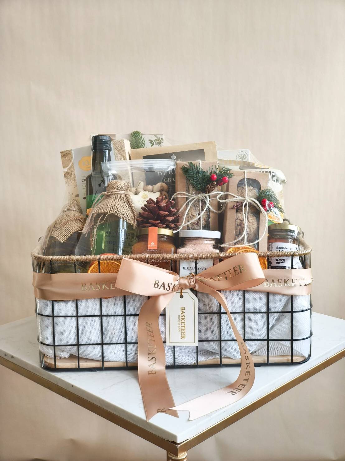 Luxury gourmet gift basket with premium snacks, drinks, Himalayan salt, and festive decorations in a wire-frame hamper with satin ribbon.