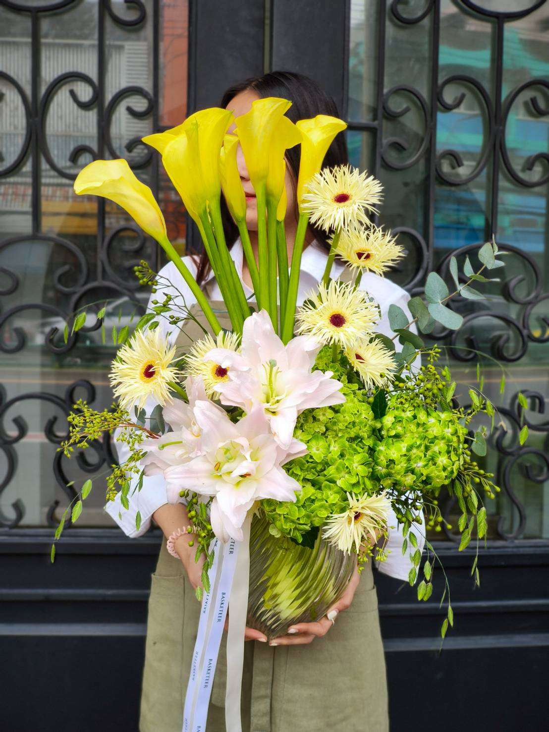 Luxury glass vase with yellow calla lilies, pink lilies, green hydrangeas, spider chrysanthemums, and eucalyptus leaves.