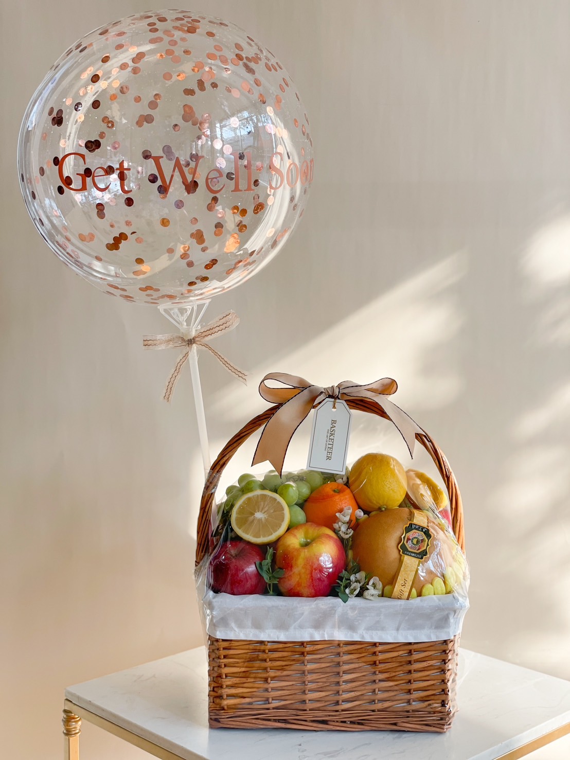 A beautifully arranged Get Well Soon Fruit Basket, featuring fresh apples, oranges, grapes, and citrus, wrapped elegantly with a confetti balloon for a cheerful recovery gift.
