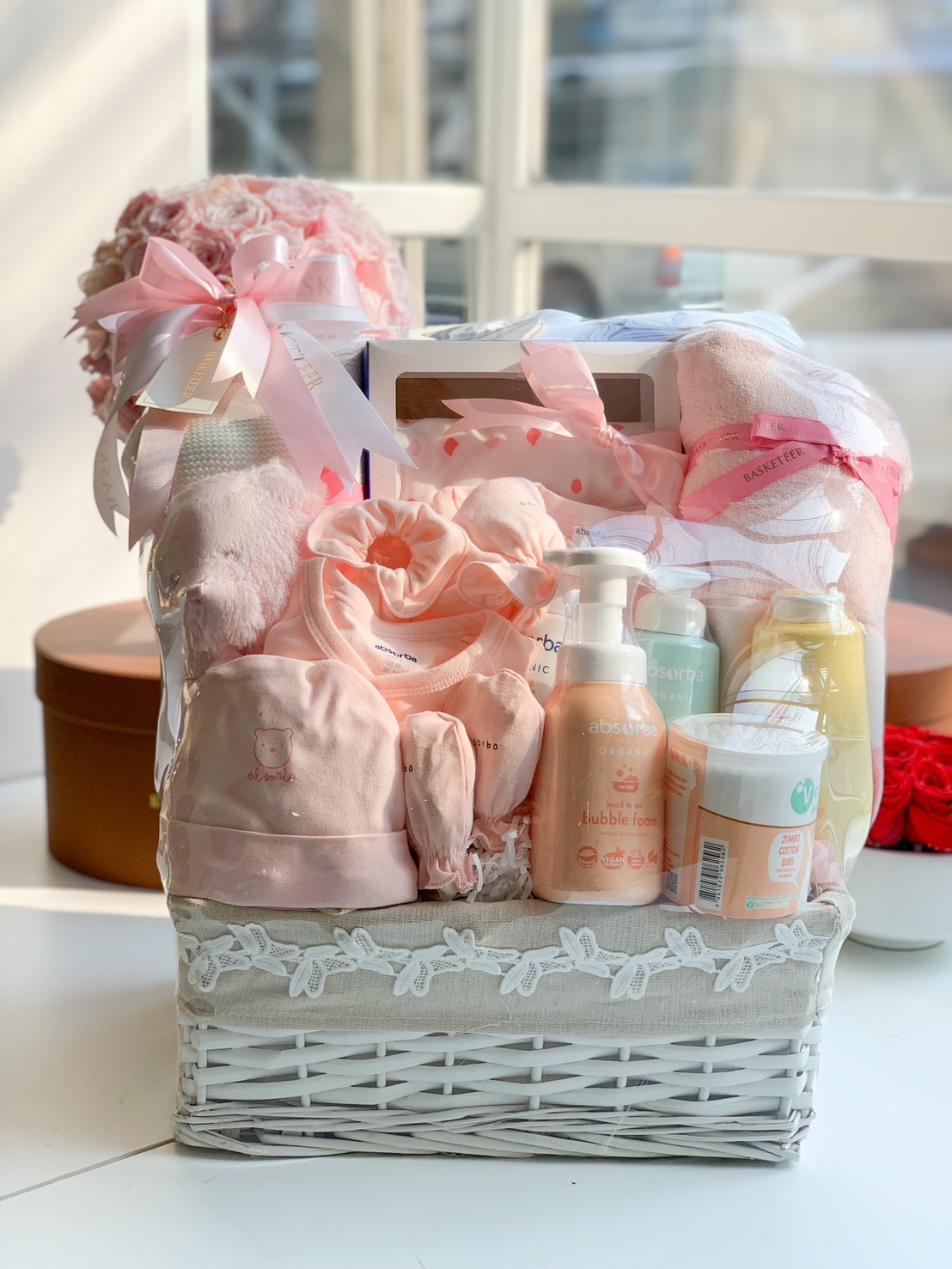 A luxury newborn baby gift basket in soft pink, featuring adorable baby clothes, plush toys, organic baby care products, blankets, and accessories, beautifully presented for the perfect baby shower gift.