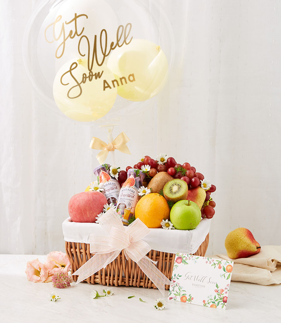 A Brown Rattan Gift Basket Filled with many different types of fresh fruits such as red apples, red grapes, oranges, etc. and refreshing fruit juices. With bright balloons with names and the words 