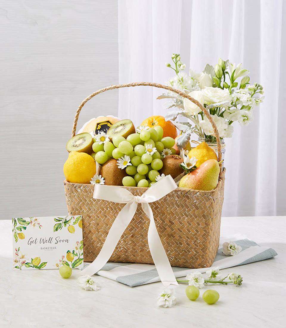 Fresh Fruits In Woven Basket With A Small White Flowers In Vase