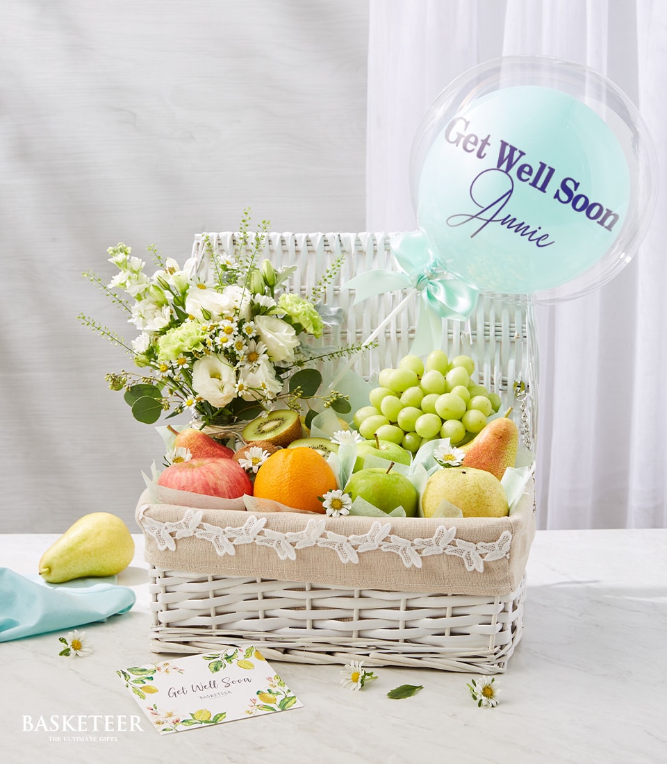 Fresh Fruits And Blue Get Well Soon Balloon In The White Hamper With A Small White Flowers Vase
