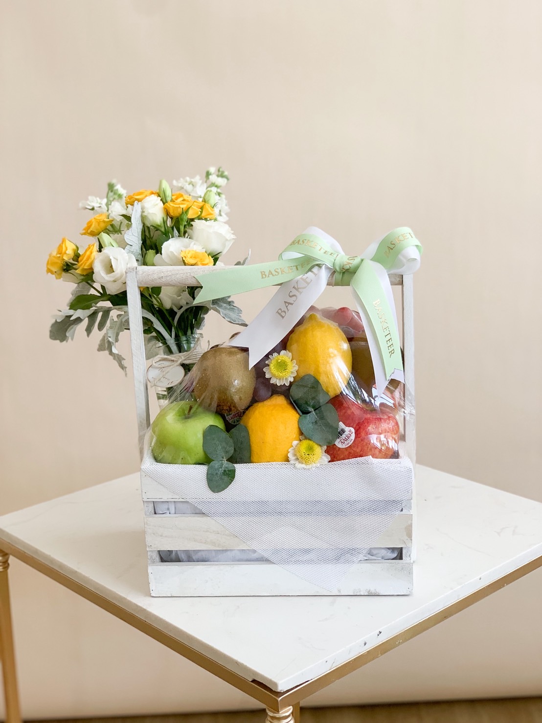 Luxury fresh fruit basket in a white wooden crate, decorated with flowers and green ribbon – perfect healthy gift set.
