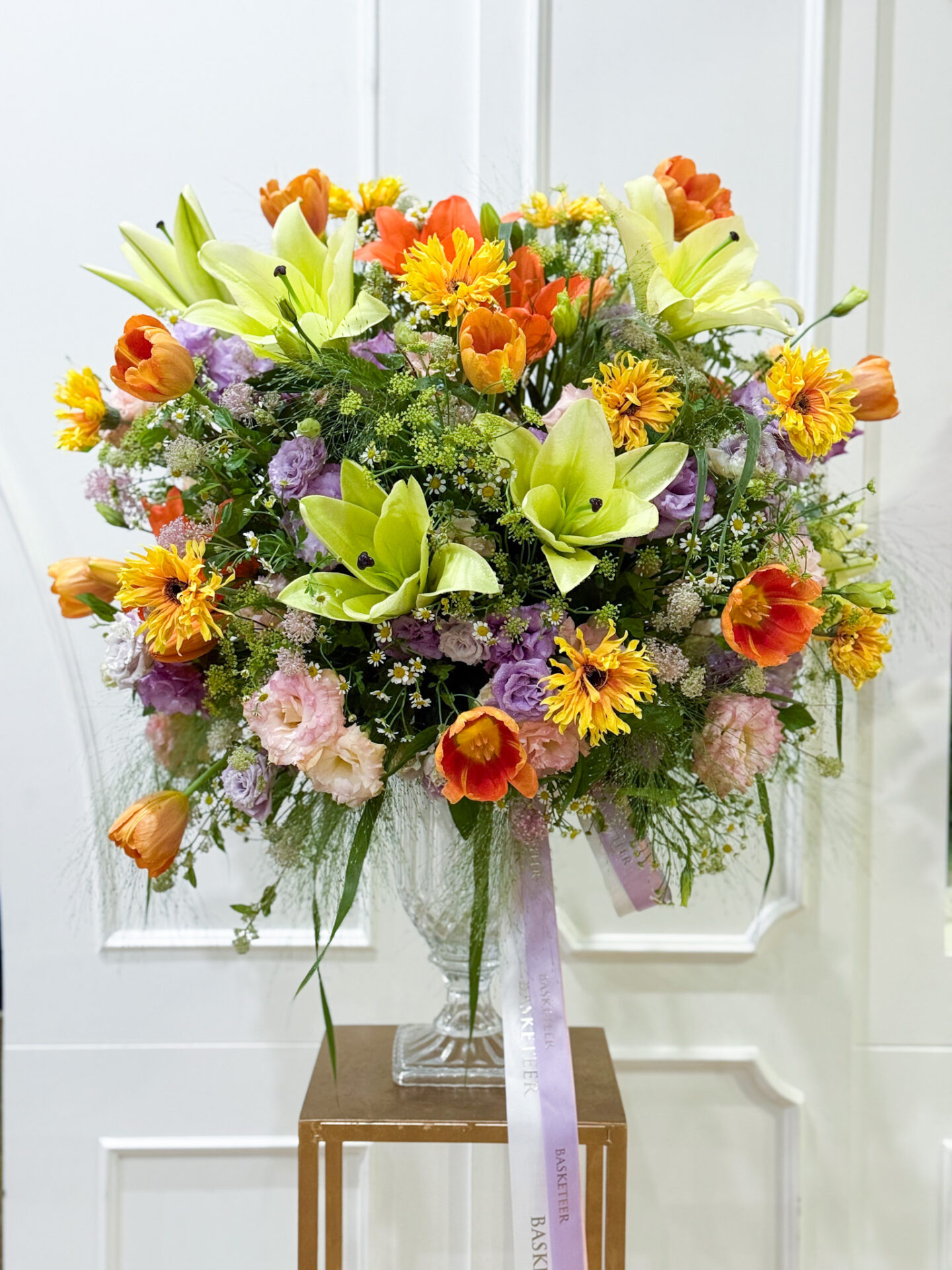Luxury vase arrangement with orange tulips, yellow chrysanthemums, green lilies, purple lisianthus, and pink roses, styled elegantly.