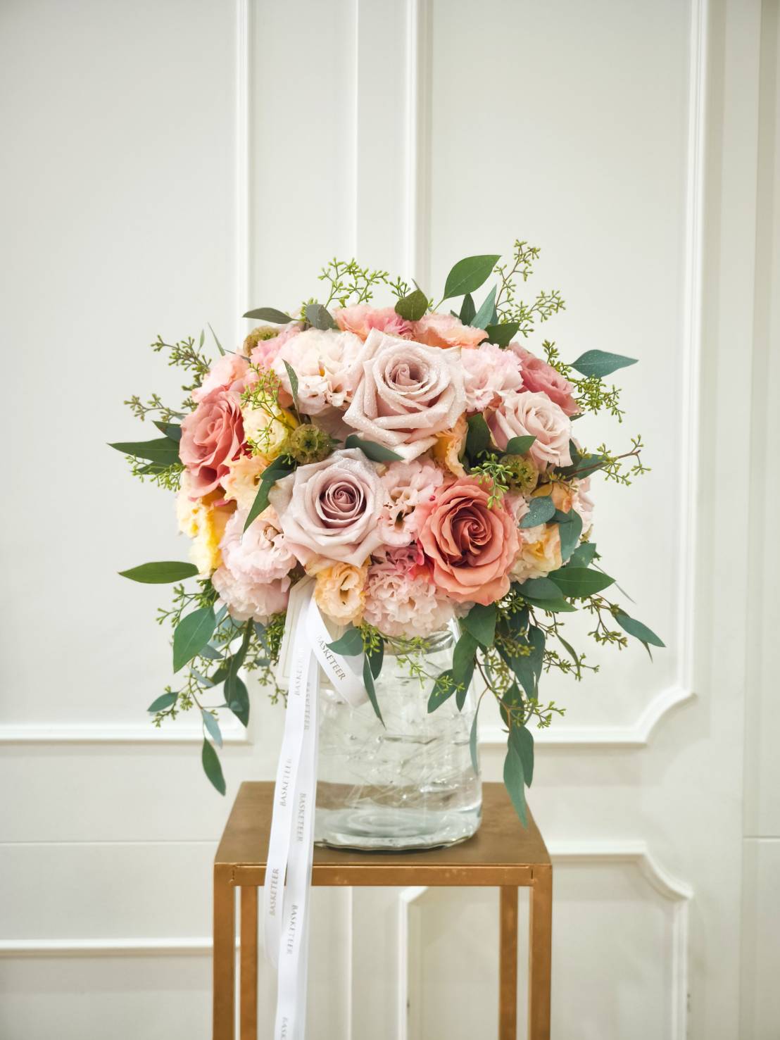 Luxury glass vase filled with peach, blush, and dusty pink roses, accented with greenery and delicate filler flowers.
