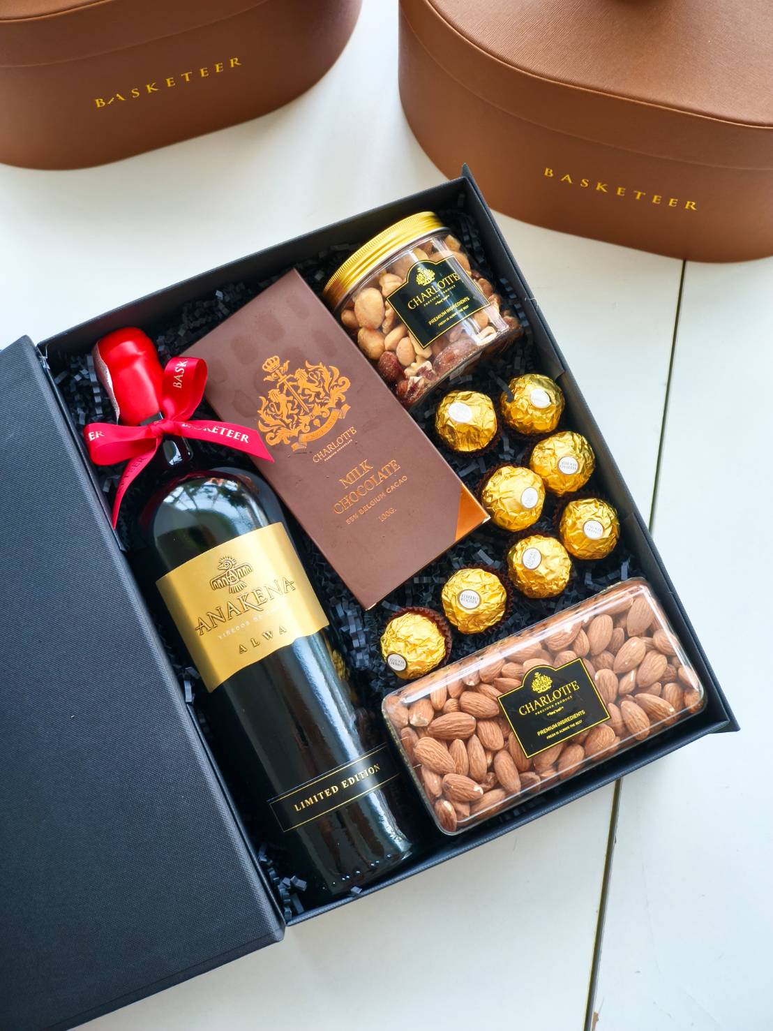 Luxury gift box with red wine, assorted chocolates, whole almonds, and mixed nuts in premium Basketeer packaging.