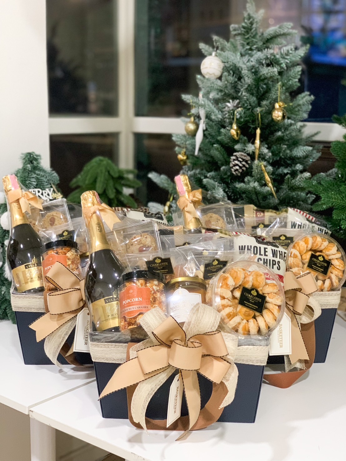 Luxurious gift hamper with prosecco, popcorn, cookies, and gourmet treats in a navy basket with a festive bow.