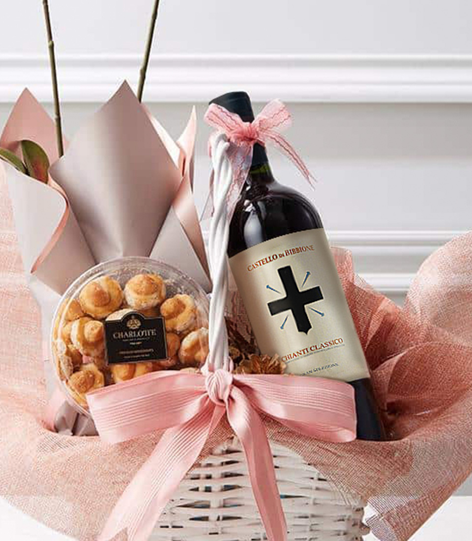 Close-up of a sophisticated gift basket featuring a bottle of red wine, a delicate orchid plant, and gourmet pastries, elegantly wrapped in pink fabric with a satin bow.