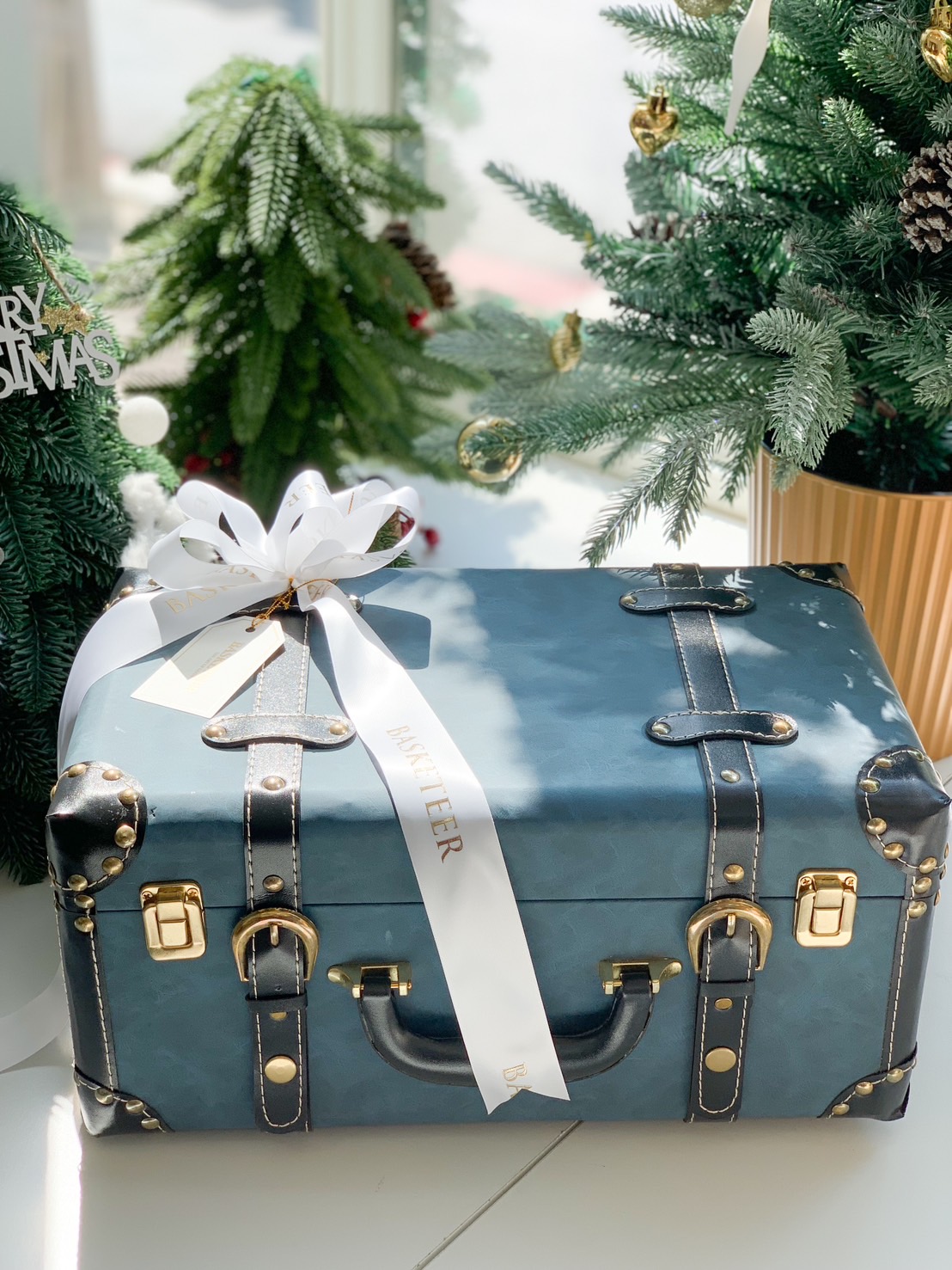 Open vintage blue leather trunk filled with gourmet treats, including chocolates, nuts, and pastries, against a festive Christmas background.