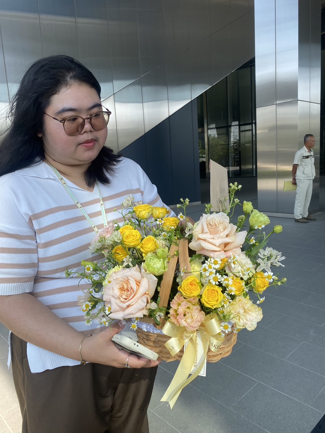 A wicker basket filled with yellow roses, pastel blooms, and daisies, held by a customer by Basketeer.