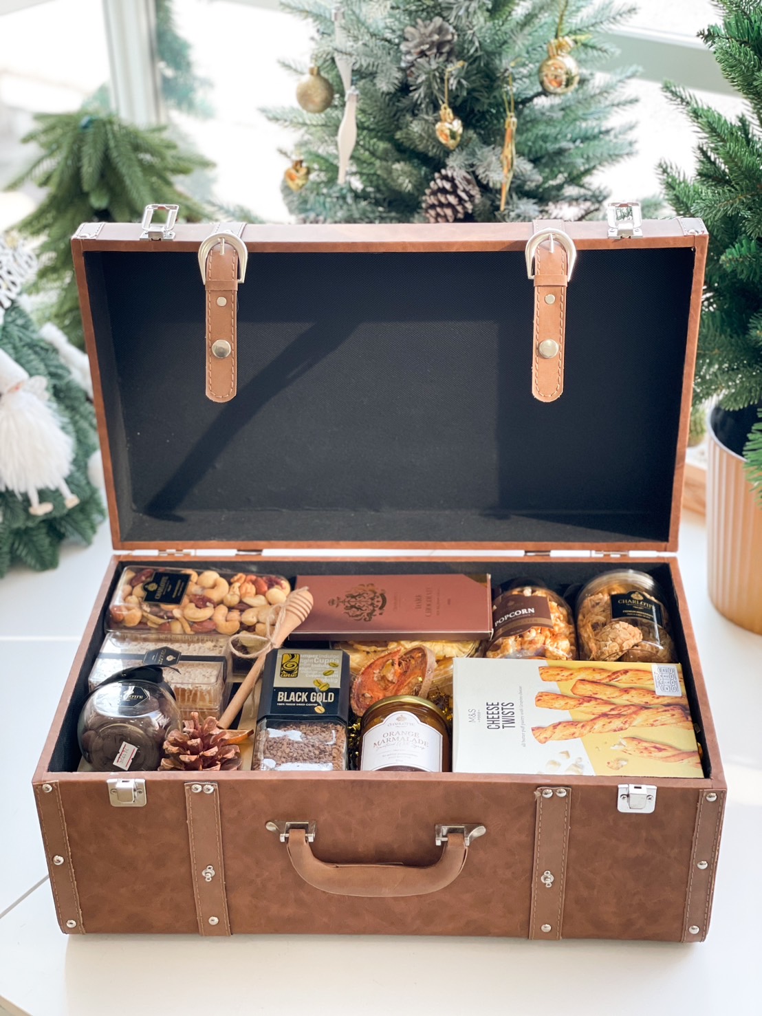 Open luxury leather chest filled with gourmet items including chocolates, mixed nuts, marmalade, popcorn, and savory cheese twists.