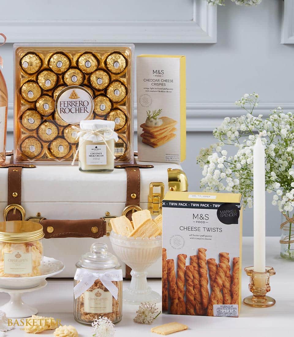 A luxurious gift arrangement exquisitely curated by Basketeer, featuring indulgent Ferrero Rocher chocolates, an opulent white candle, savory cheese crisps and twists, a delectable jar of biscuits, and tangy lemon curd. All items are elegantly displayed against an immaculate white backdrop adorned with delicate baby's breath flowers for a touch of timeless elegance. The scene is completed with Basketeer's signature ribbon and box, adding an extra layer of sophistication and charm.