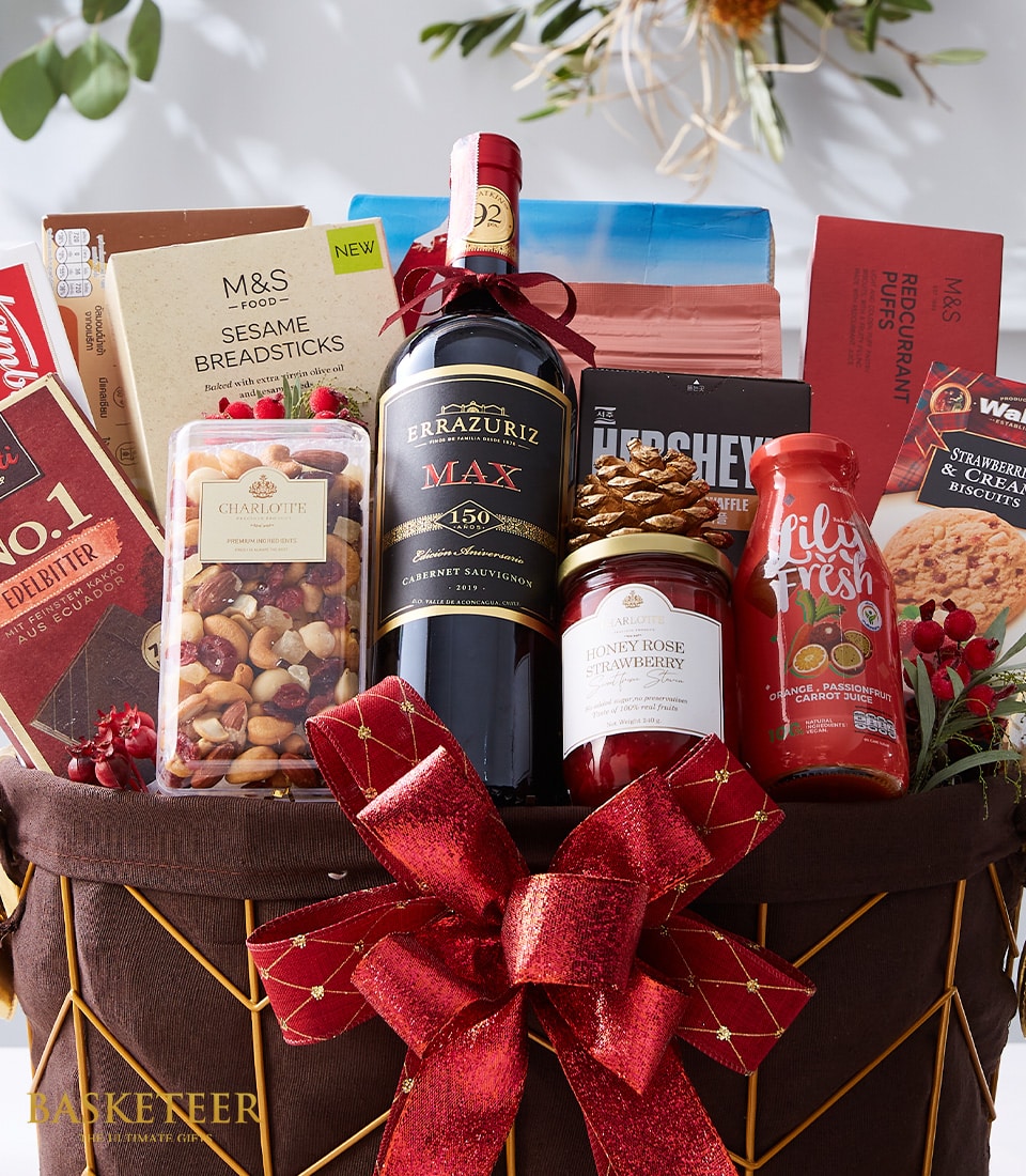 The Champagne & Gourmet Delights Basket, an exquisite offering from Basketeer, presents an array of luxurious snacks and beverages. This lavish basket features a bottle of distinguished Errazuriz Max wine, elegant M&S sesame breadsticks, decadent chocolate, luscious strawberry honey, and handcrafted red sauce among other gourmet treats. Meticulously adorned with a sumptuous red ribbon and festive decorations, the basket exudes sophistication and invites indulgence. The Basketeer branding adds an extra touch of refinement to this perfect gift for any discerning connoisseur.