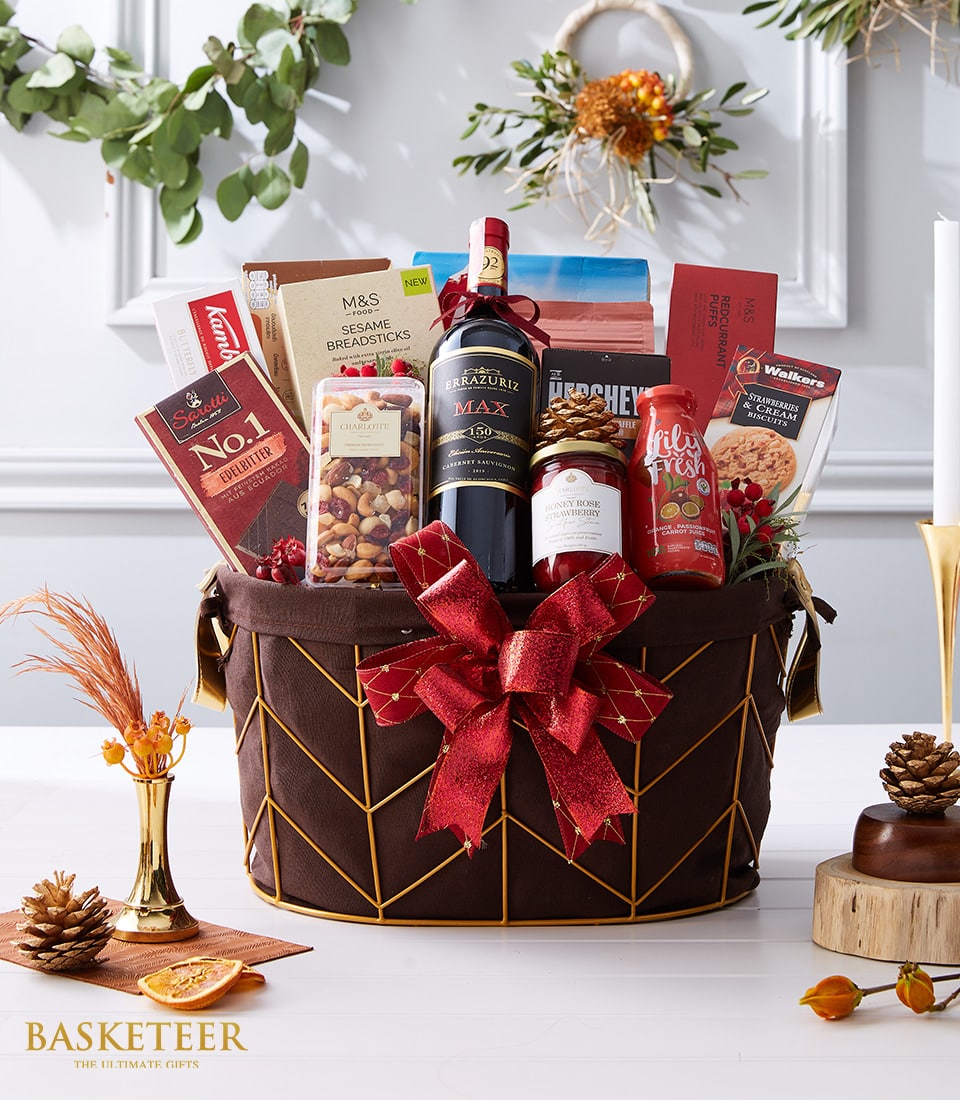 Festive brown-gold basket with Cabernet Sauvignon wine, chocolates, mixed nuts, jam, juice, breadsticks, and red bow