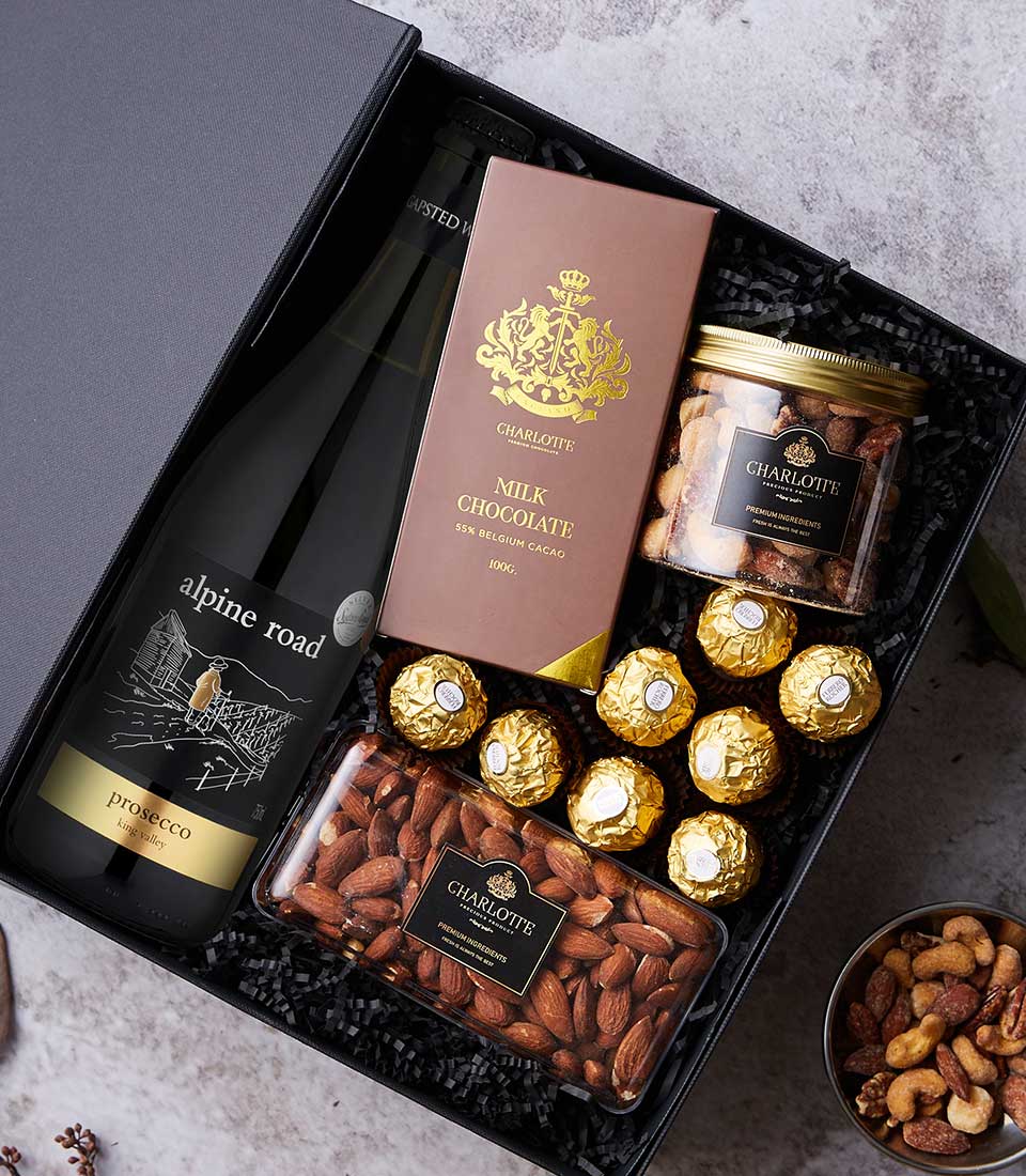 Indulge in a luxury gift hamper with Alpine Road Prosecco, Charlotte chocolate, nuts, and Ferrero Rocher on elegant black shred.