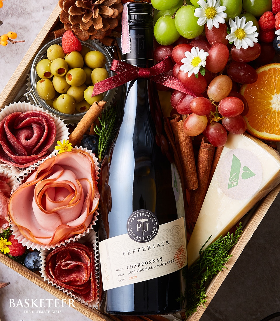 The Basketeer gourmet gift box is an epitome of sophistication and indulgence. It showcases a distinguished bottle of Pepperjack Chardonnay, nestled amidst an array of exquisite cheeses, premium olives, lush grapes, succulent strawberries, and artfully crafted salami roses. The arrangement is delicately garnished with fragrant flowers and aromatic cinnamon sticks to elevate the sensory experience. Presented in a chic box adorned with the prestigious Basketeer logo and satin ribbon, this luxurious ensemble promises to delight and impress at any occasion.