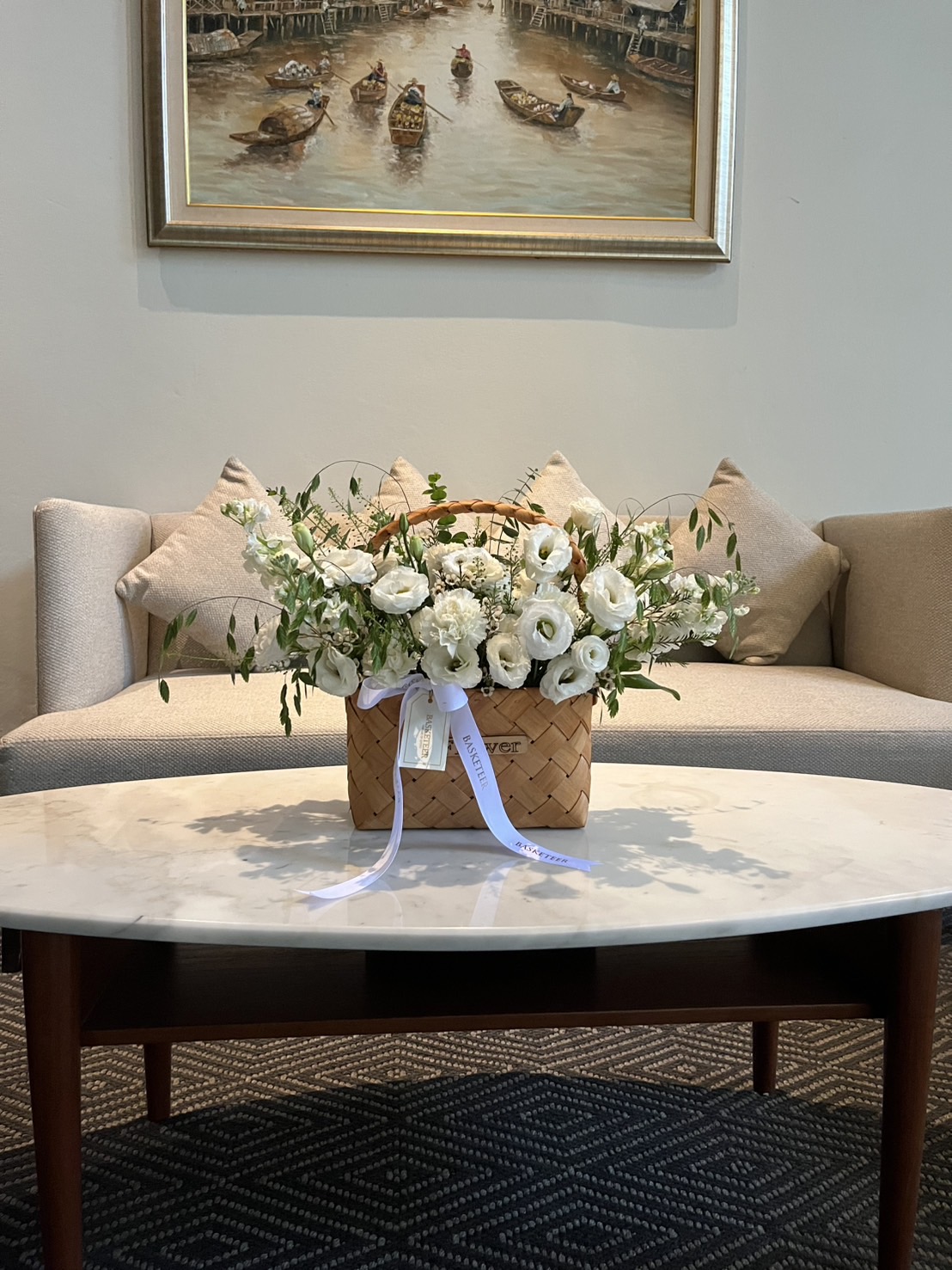 Natural woven basket with white roses, lisianthus, carnations, and eucalyptus leaves, decorated with a satin ribbon.